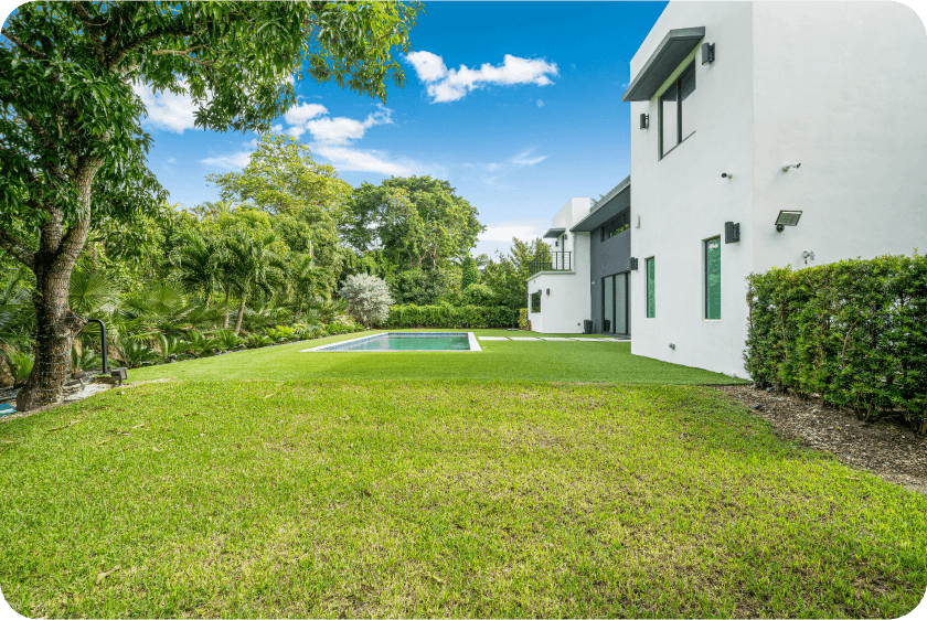 Luxurious backyard with infinity pool and modern white facade surrounded by lush palm trees in Pinecrest estate