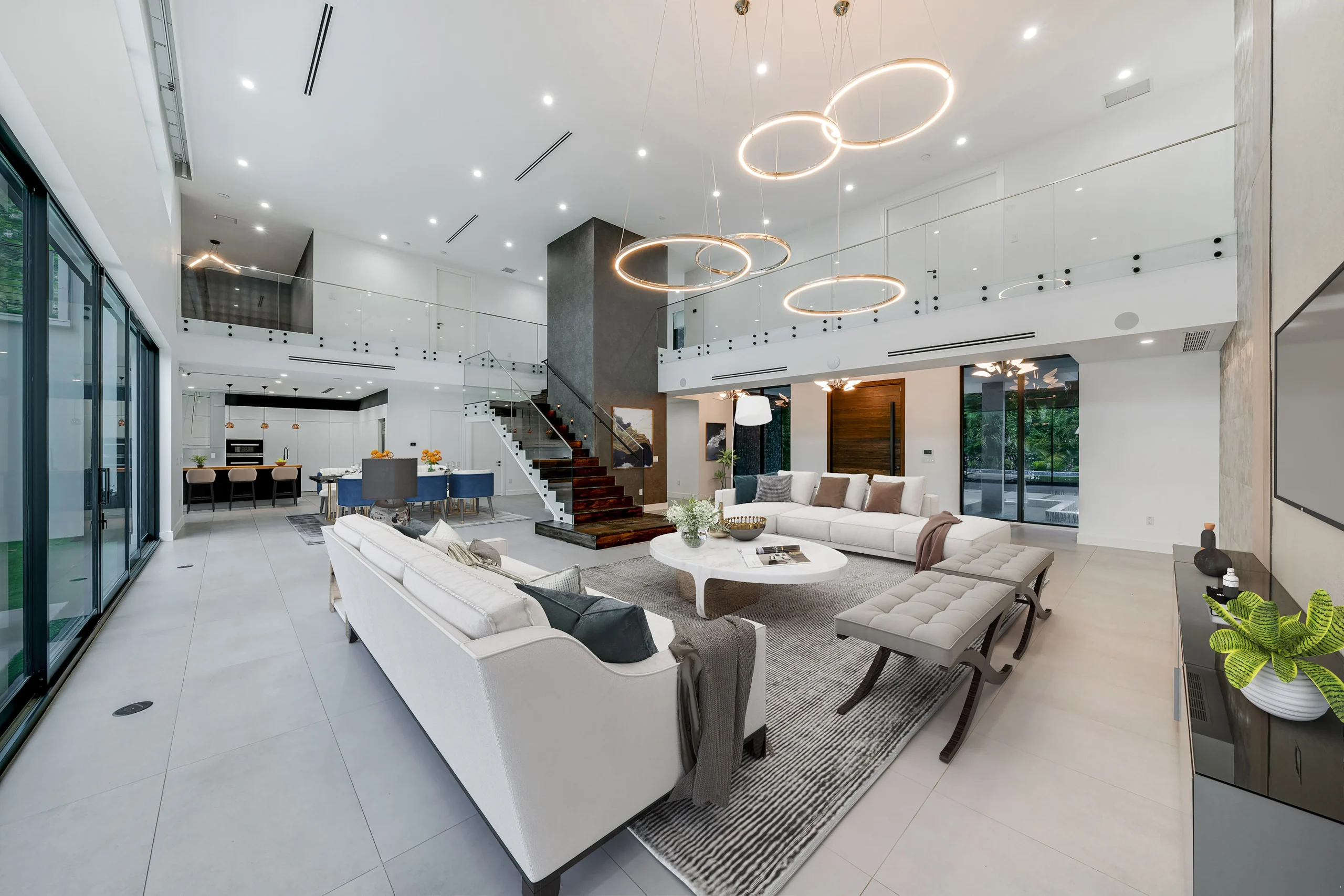 Spacious luxury living room with high ceilings, floor-to-ceiling windows, and modern pendant lighting in exclusive Pinecrest home